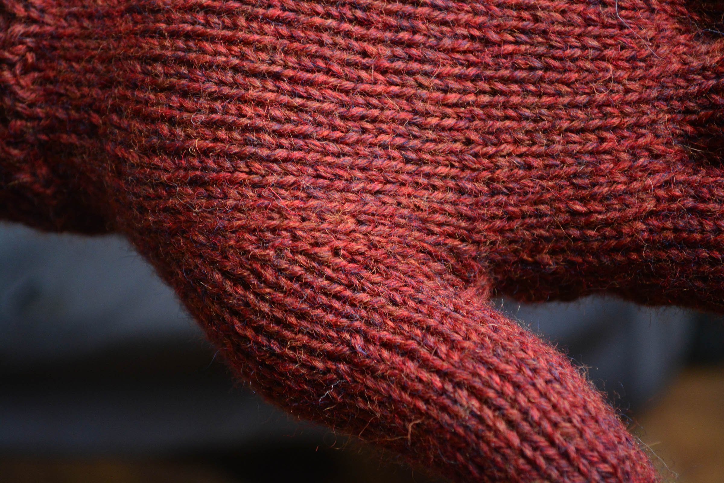 Close-up of the palm side of a thumb gusset on worsted-weight gloves being modelled on a man's hand.