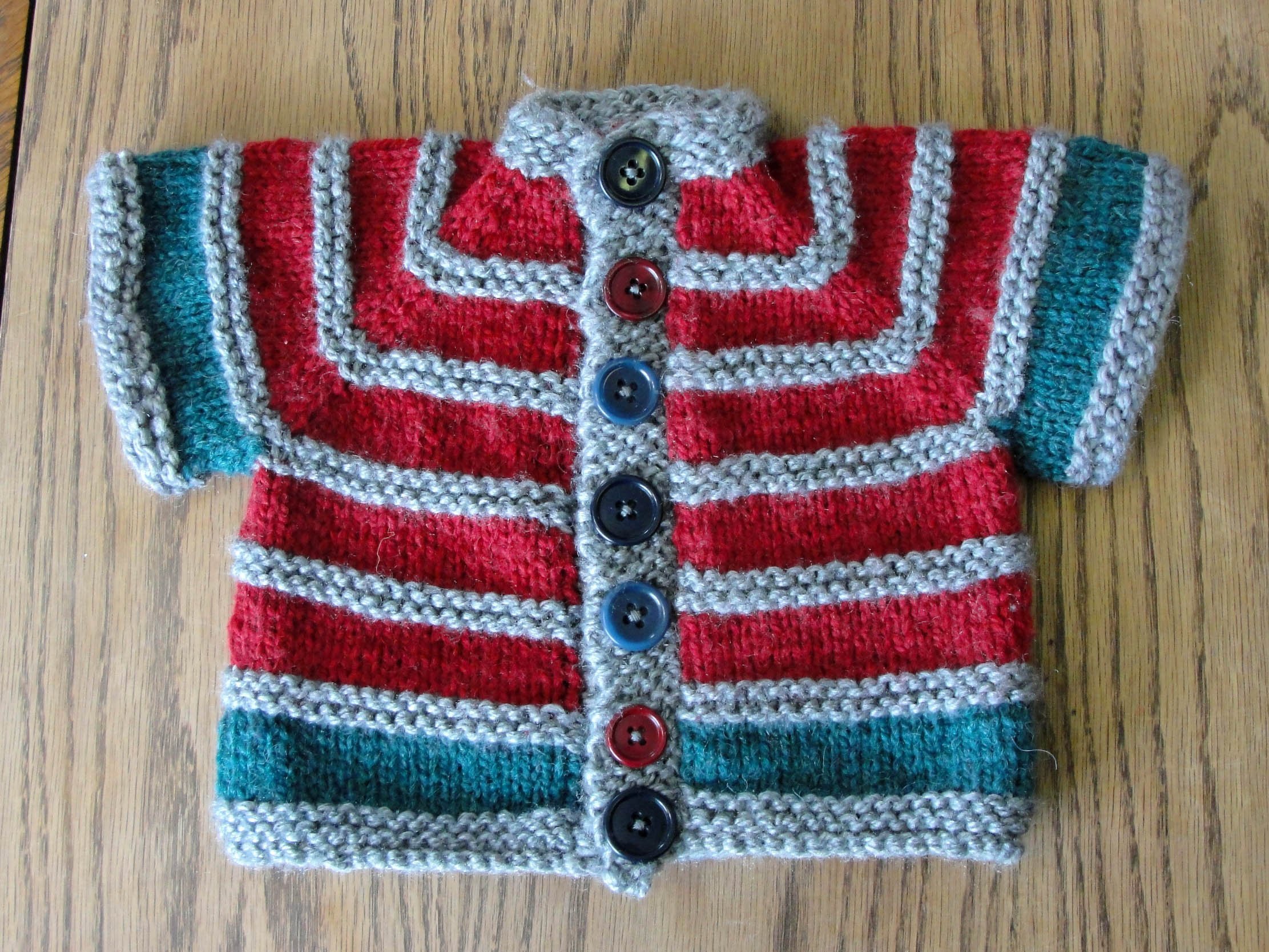Flat lay of a short-sleeved baby cardigan with alternating garter stitch and stockinette stripes that uses raglan shoulder shaping.