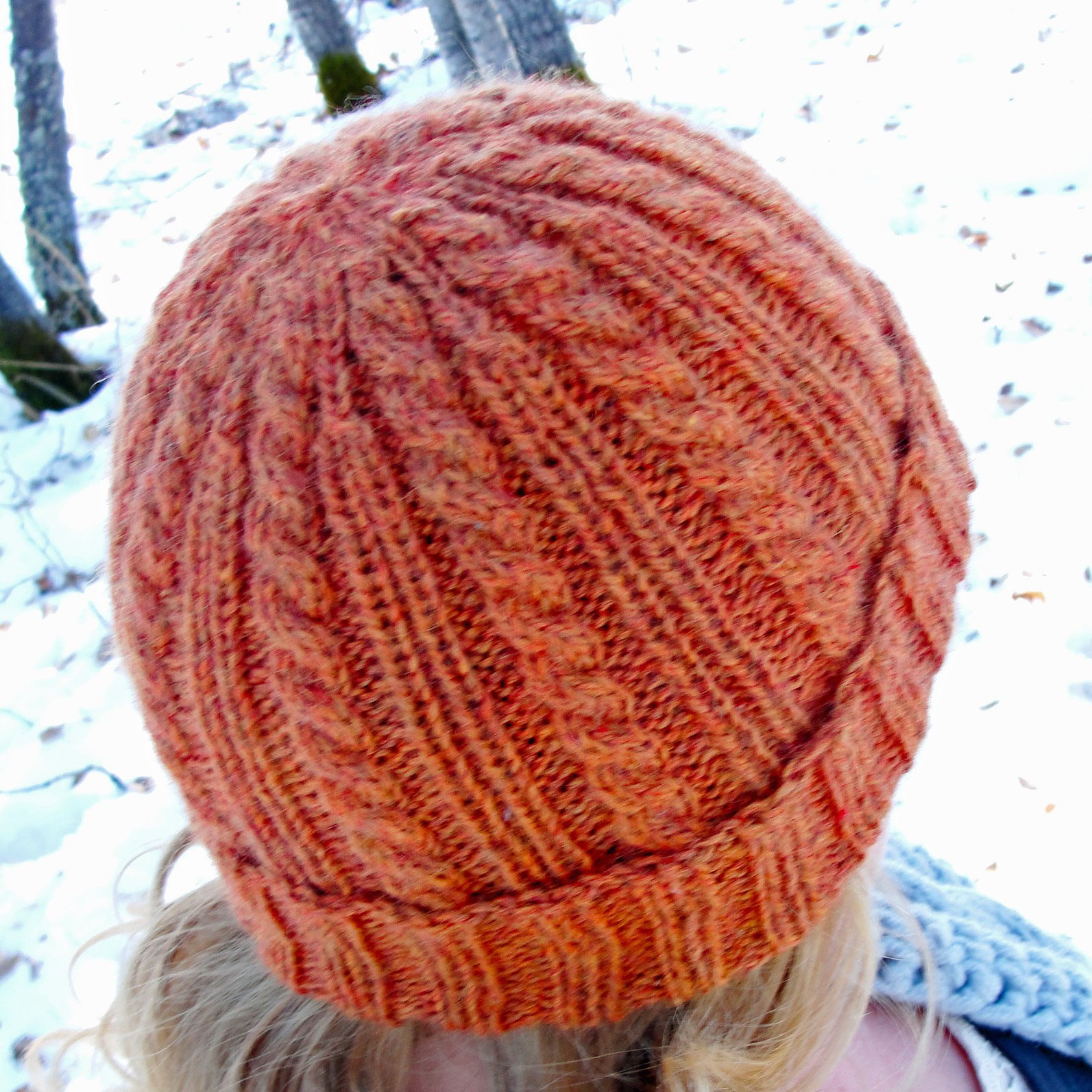 Crown of a cabled and ribbed rolled-brim beanie showing double rib columns merging into one and cables narrowing at the top.
