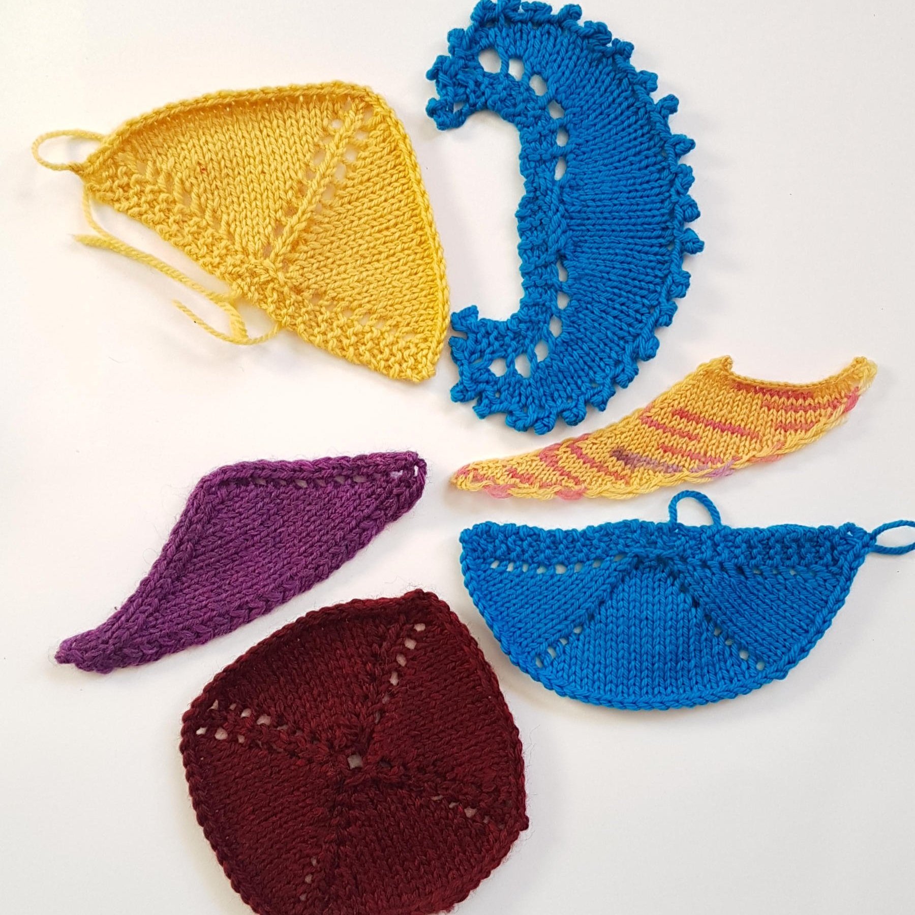 Six blocked shawl swatches of various styles are gathered in a group.